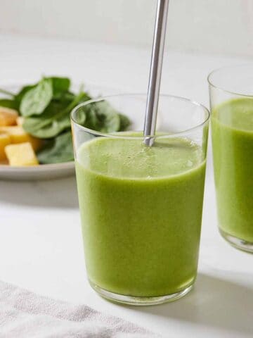 A glass of green smoothie with a metal straw.