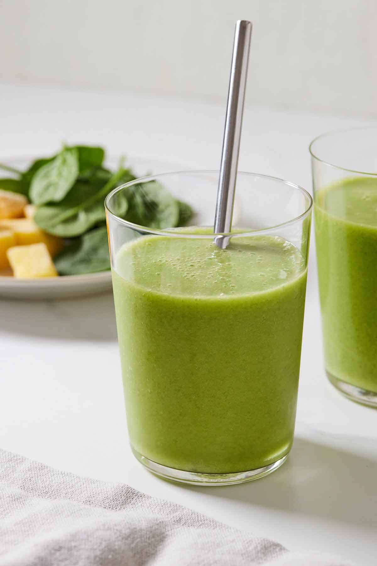 A glass of green smoothie with a metal straw.