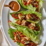 Pinterest graphic of a platter with four shrimp lettuce wraps with a bowl of sauce.