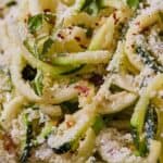 Pinterest graphic of a close up view of zucchini noodles with parmesan and red pepper flakes.