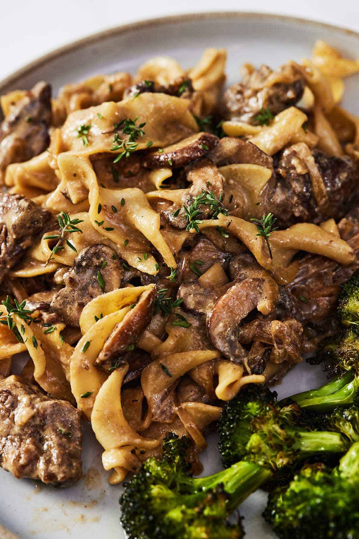 Close up of a plate of beef stroganoff with mushrooms and broccoli.