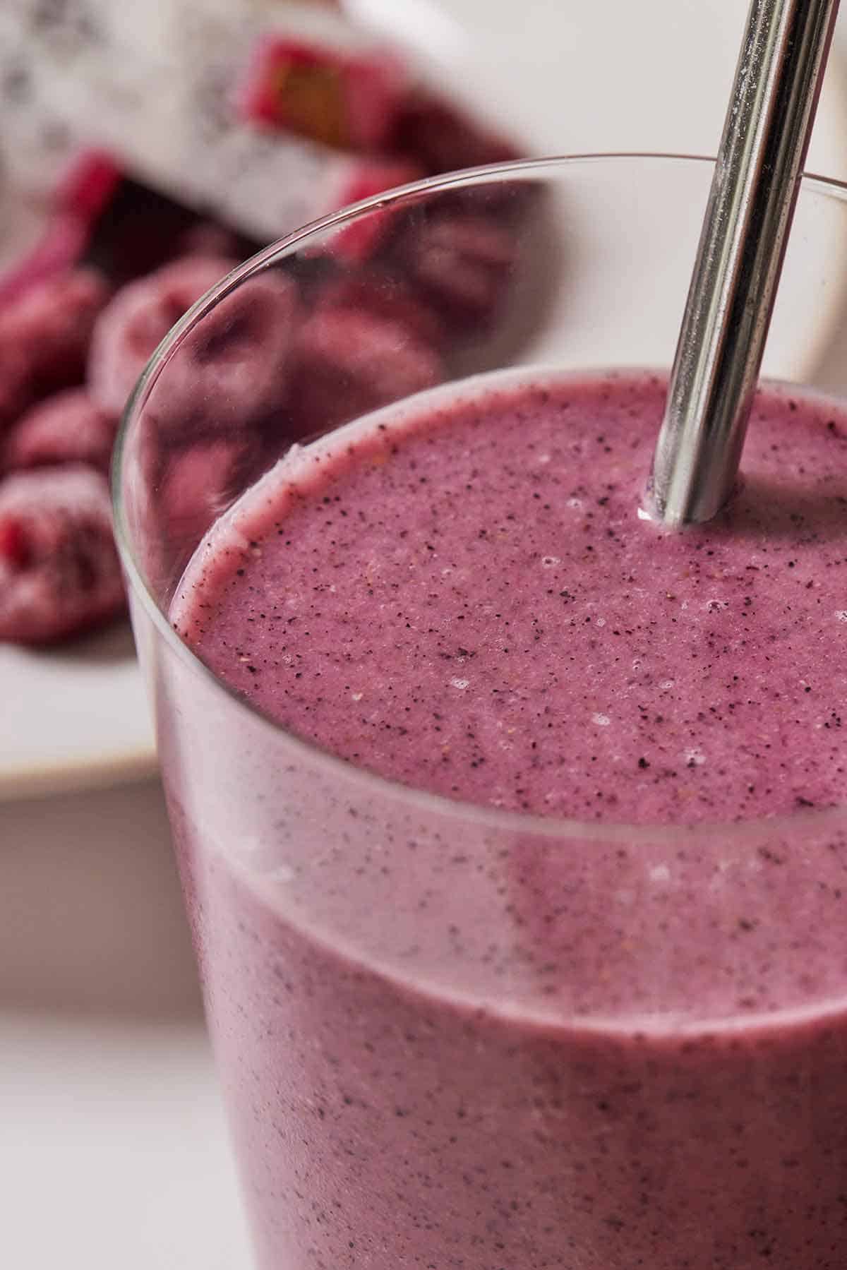 Close up view of a glass of dragon fruit smoothie with a straw.