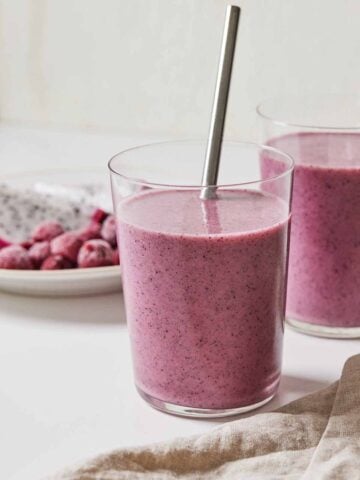 Two glasses of dragon fruit smoothie, one in front with a straw.