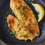 Pinterest graphic of a plate of air fryer tilapia with a wedge of lemon beside it.