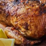 Pinterest graphic of the close up view of an air fryer roasted chicken by lemon wedges.