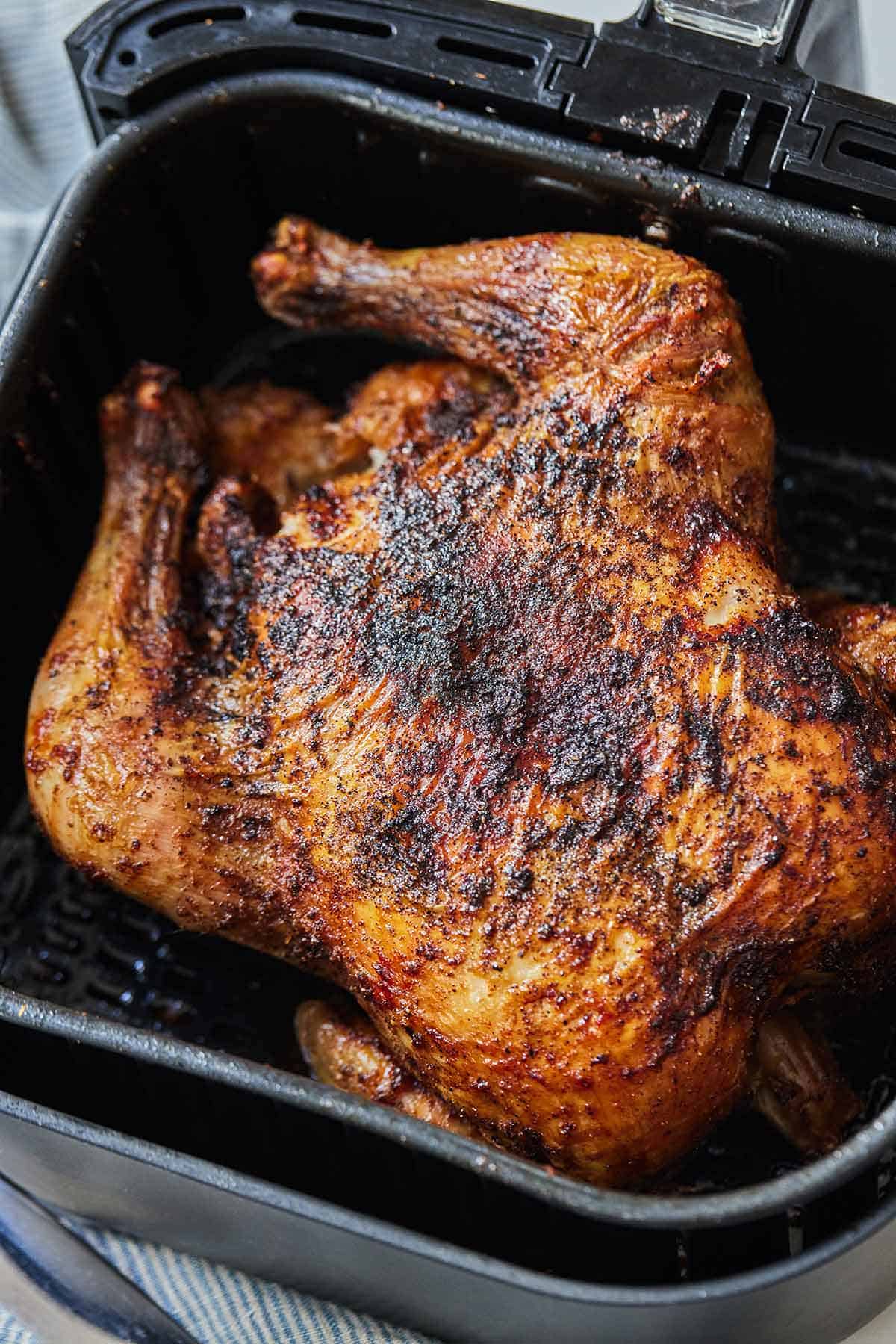 A whole roasted chicken in an air fryer basket.
