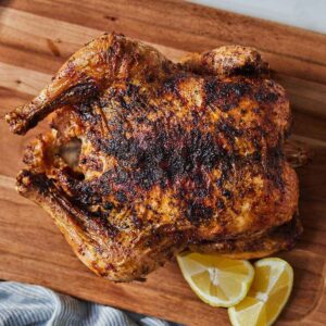 An air fryer whole chicken on a cutting board with lemon wedges beside it.