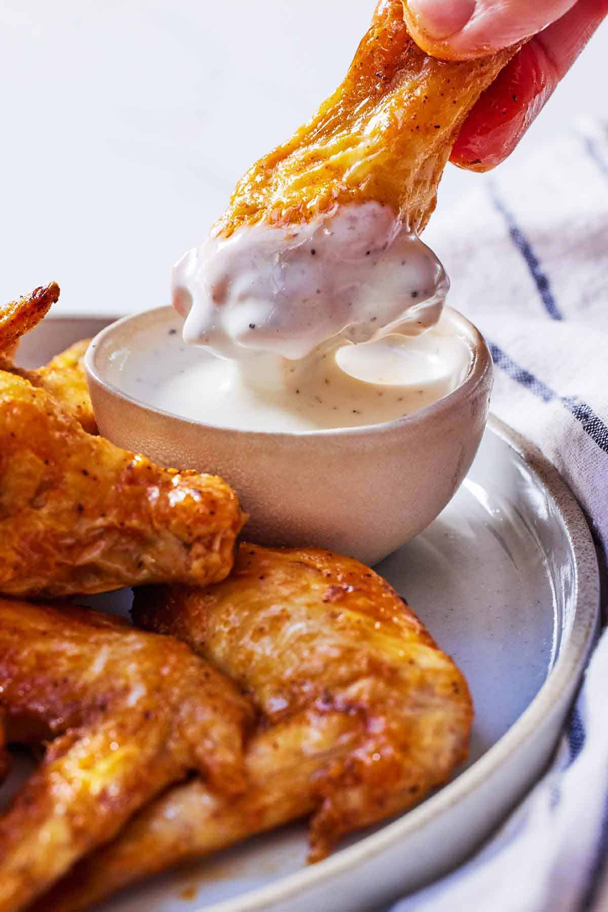An air fryer chicken wing being dipped into sauce.