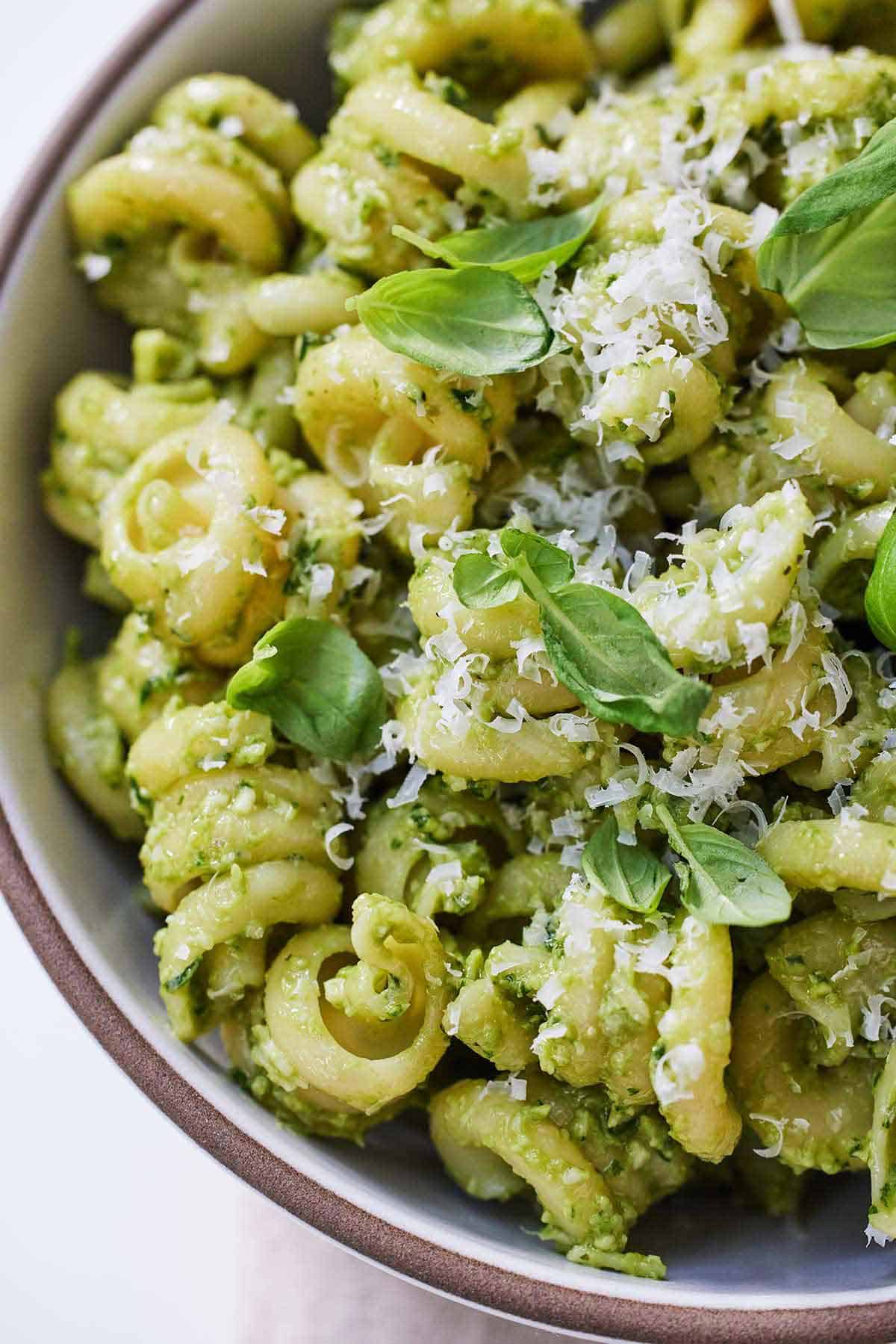 Close up of a bowl of avocado pesto pasta with fresh basil and grated parmesan on top.