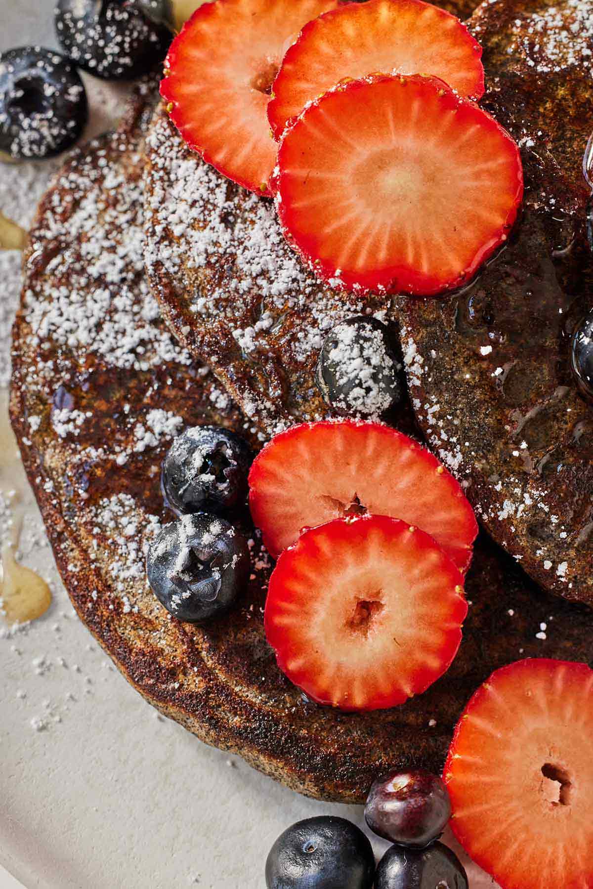 Close up of buckwheat pancakes garnished with strawberries and blueberries.