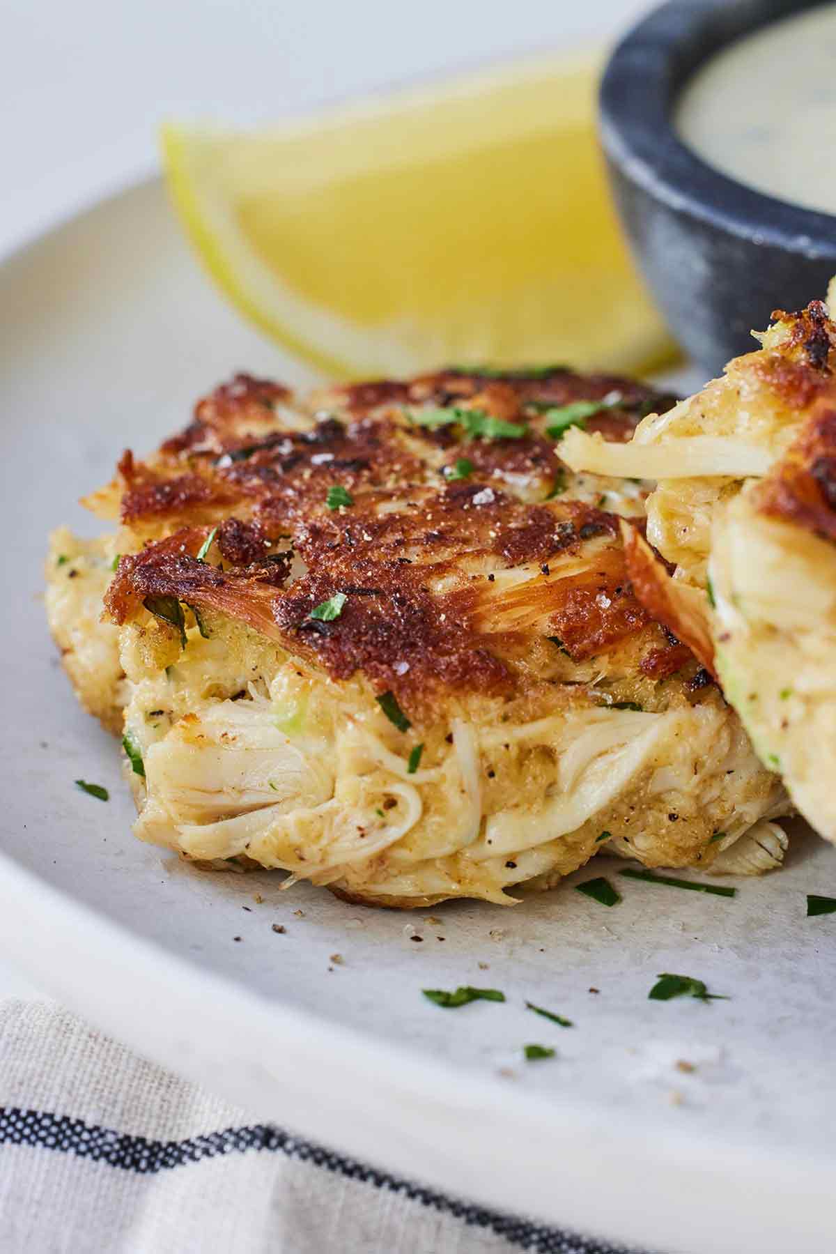 Close up of a crab cake with a lemon wedge in the background.