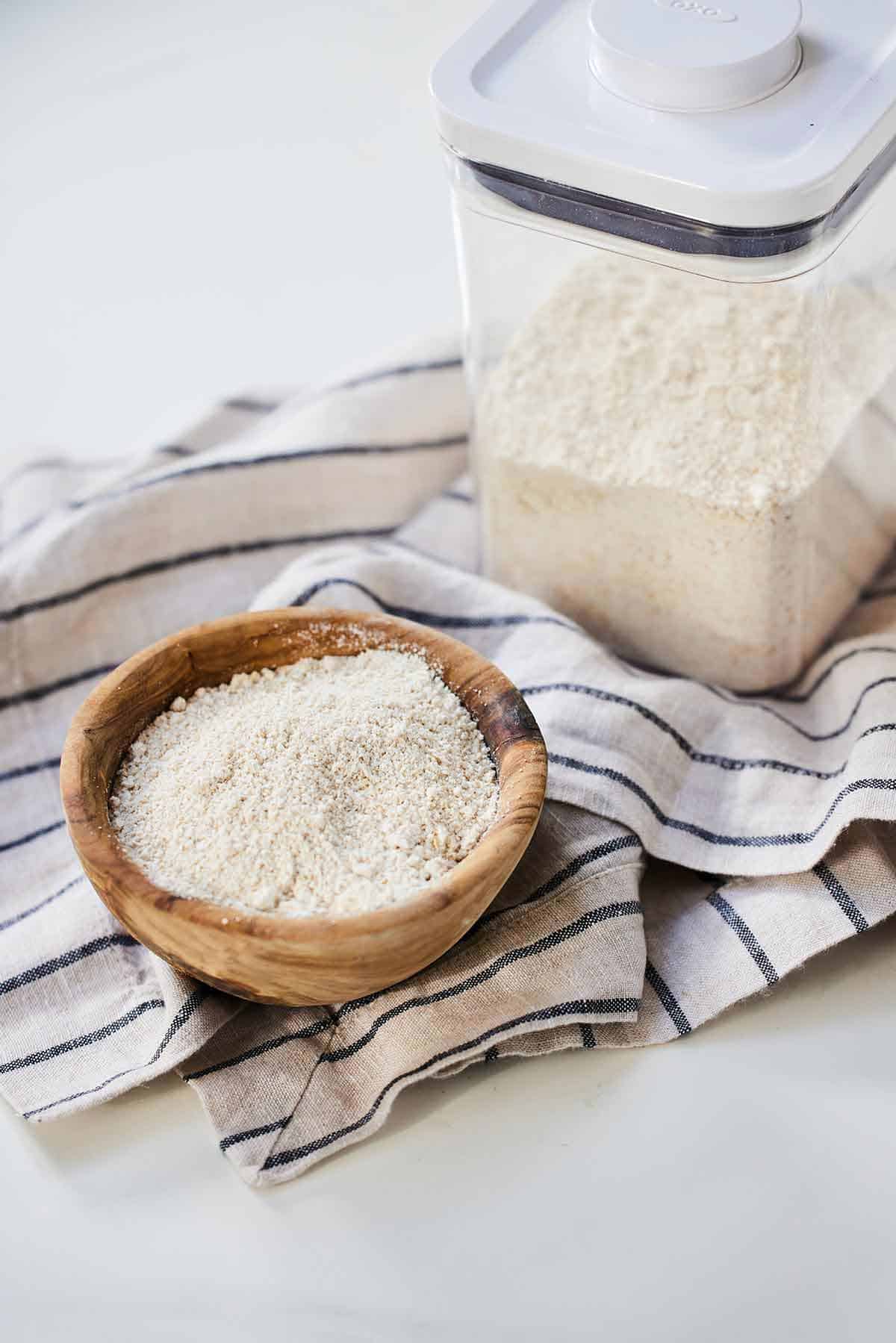 A container and bowl of oat flour on a linen napkin.