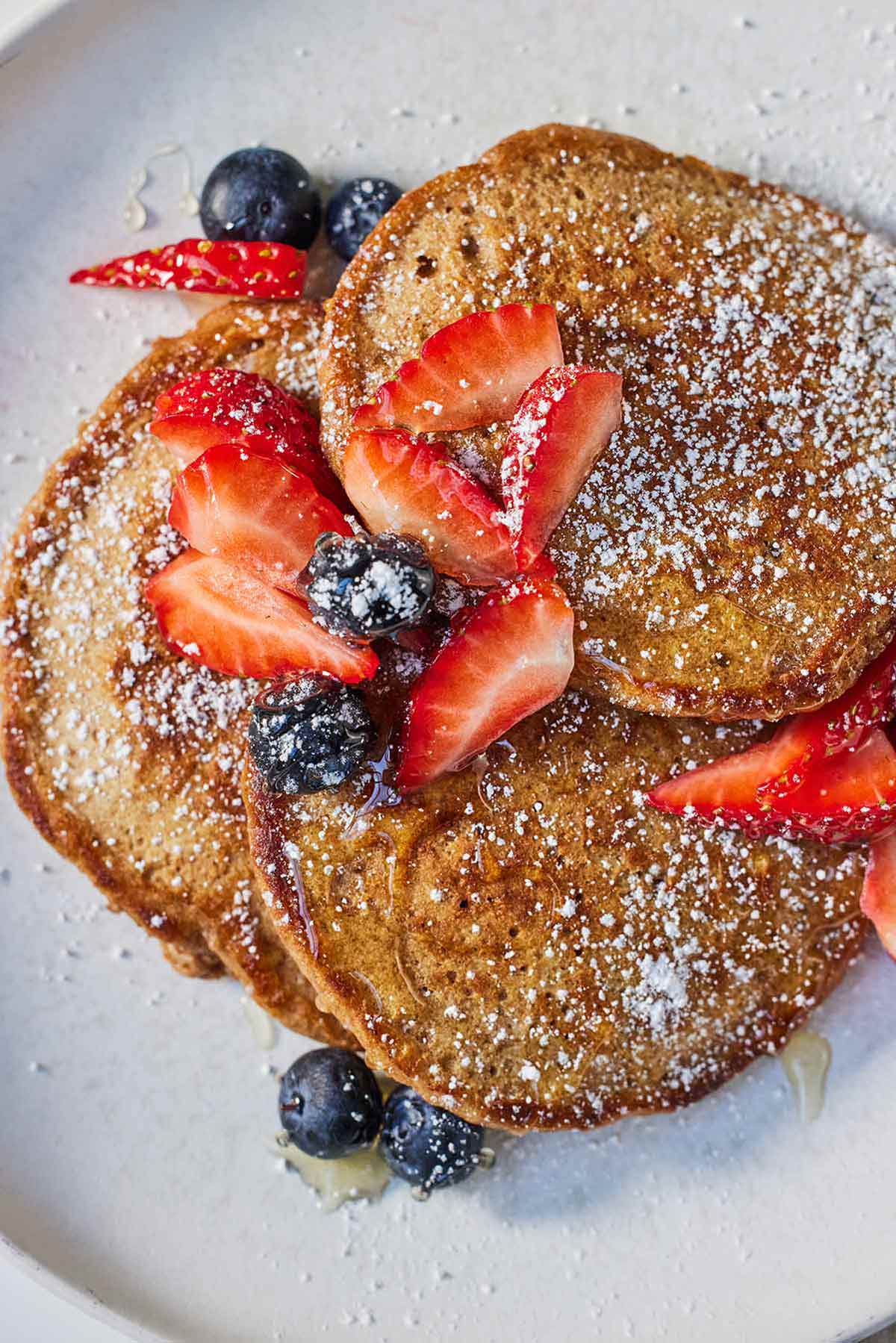Overhead view of a plate with three whole wheat pancakes with fruit on top.