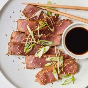 A bowl with sliced air fryer tuna steaks with soy sauce on the side with green onions on top.