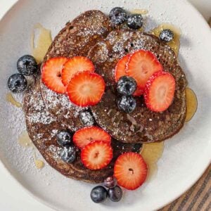 Overhead view of a plate of buckwheat pancakes with fruit on top.