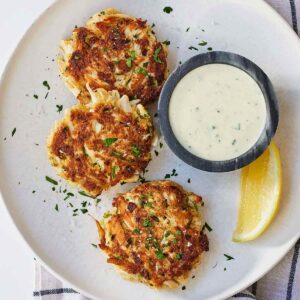 Overhead view of a plate of three crab cakes and tartar sauce.