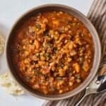 Overhead view of a bowl of lentil stew with ripped bread on the side.