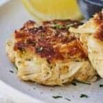 Pinterest graphic of a close view of a crab cake with a lemon wedge and sauce in the background.
