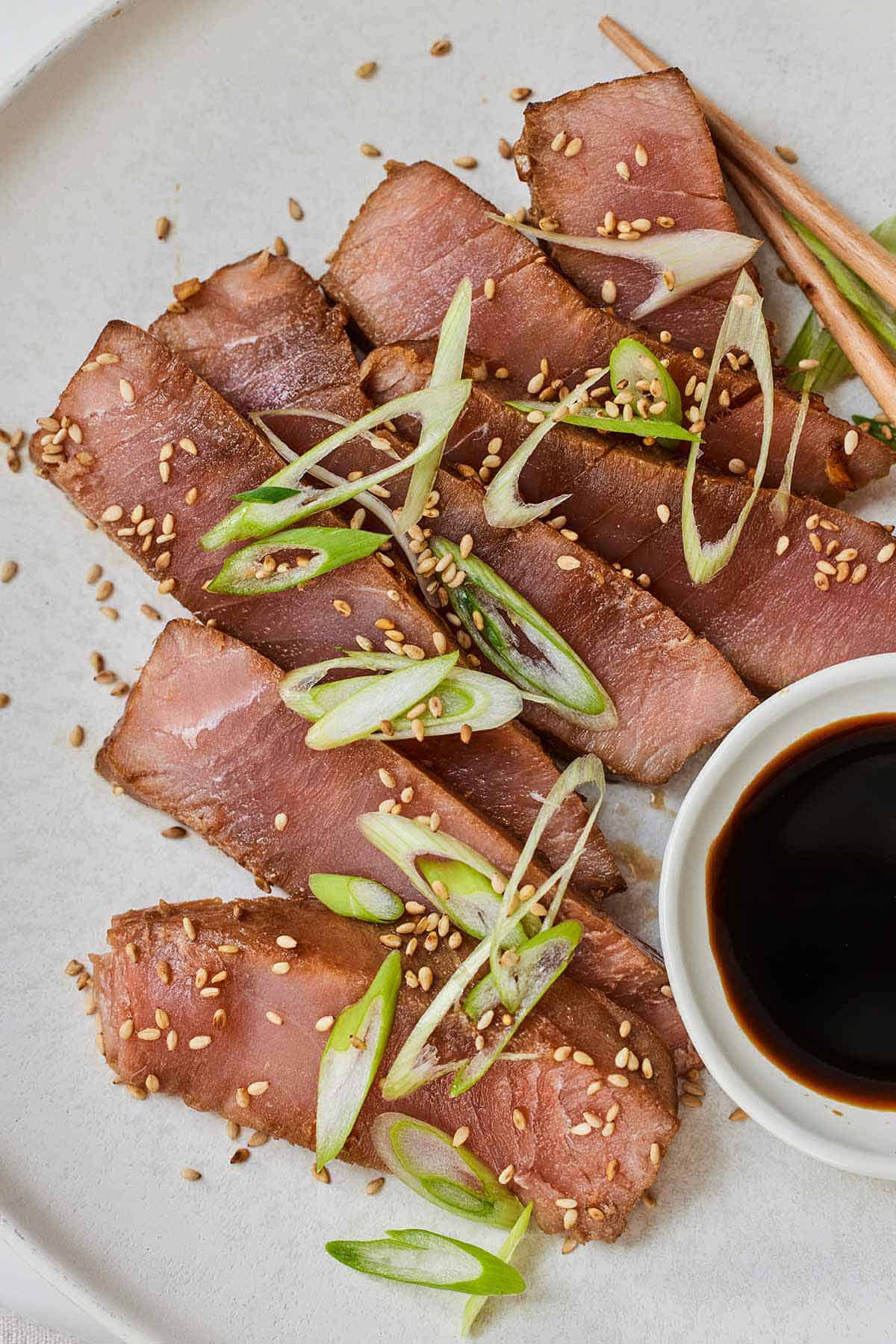 A plate with sliced air fryer tuna steaks with green onions on top.