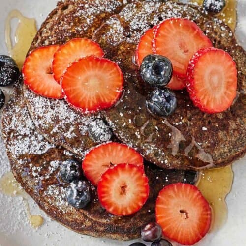 Overhead view of a plate with three buckwheat pancakes with fruit on top.