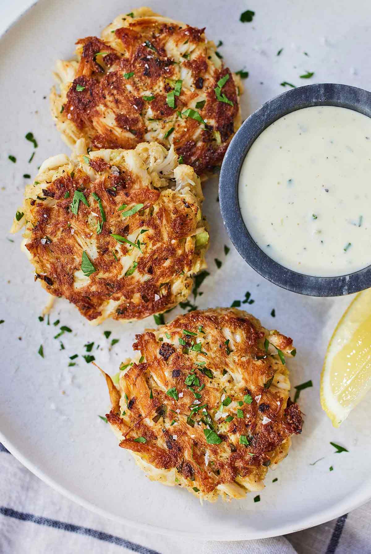 A plate with three crab cakes with a bowl of tartar sauce on the side.