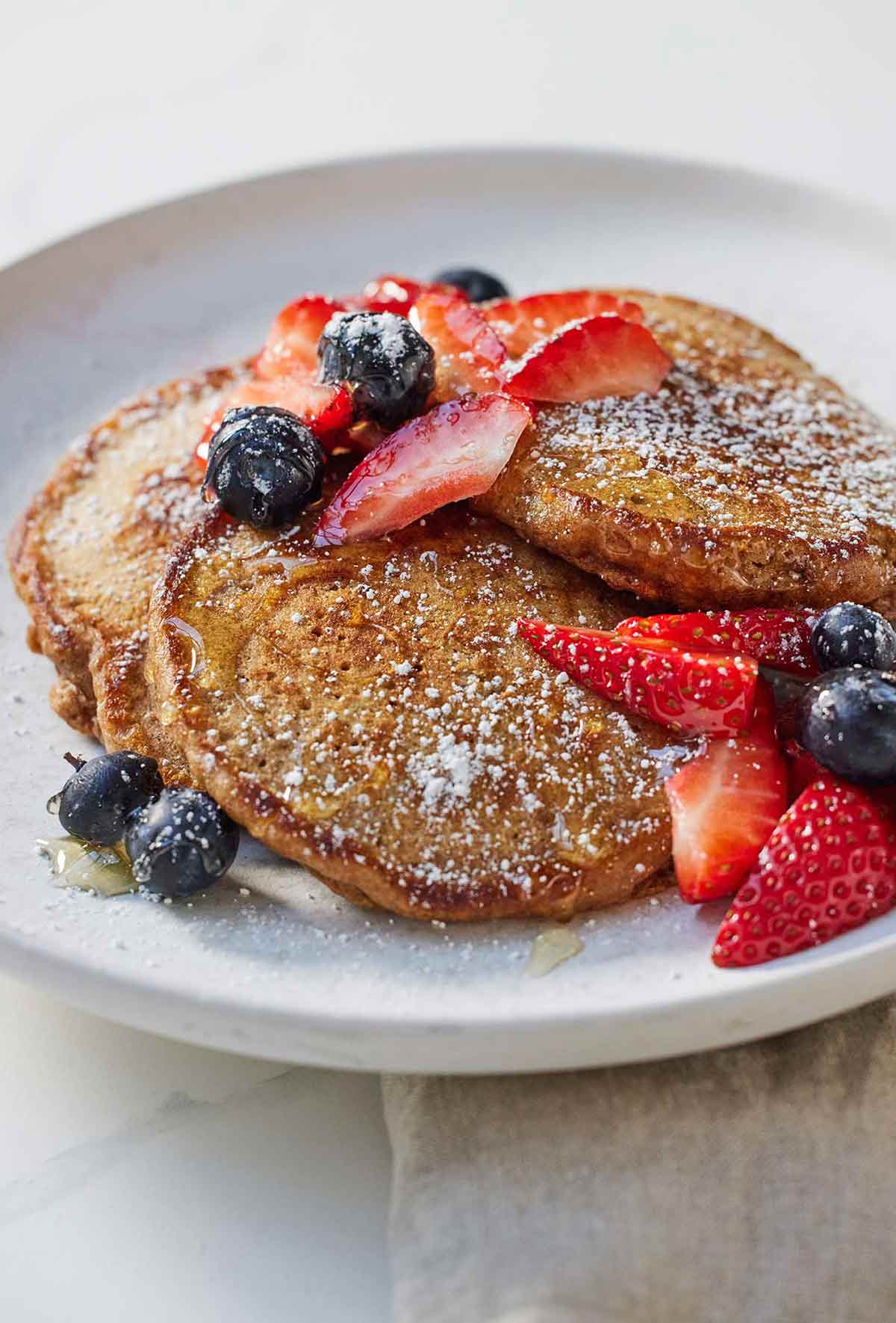 A plate with whole wheat pancakes and fresh fruit on top.