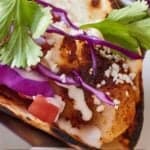 Pinterest graphic of a close up view of a fish taco with cilantro and sliced cabbage on top.