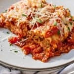 Pinterest graphic of a plate of lasagna roll ups with parmesan and basil on top.