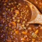 Pinterest graphic of a close up view of lentil stew with a wooden spoon.