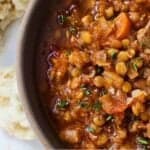 Pinterest graphic of a close view of half a bowl of lentil stew with ripped bread in the background.