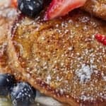 Pinterest graphic of a close up view of whole wheat pancakes with powdered sugar, syrup, and fruit.