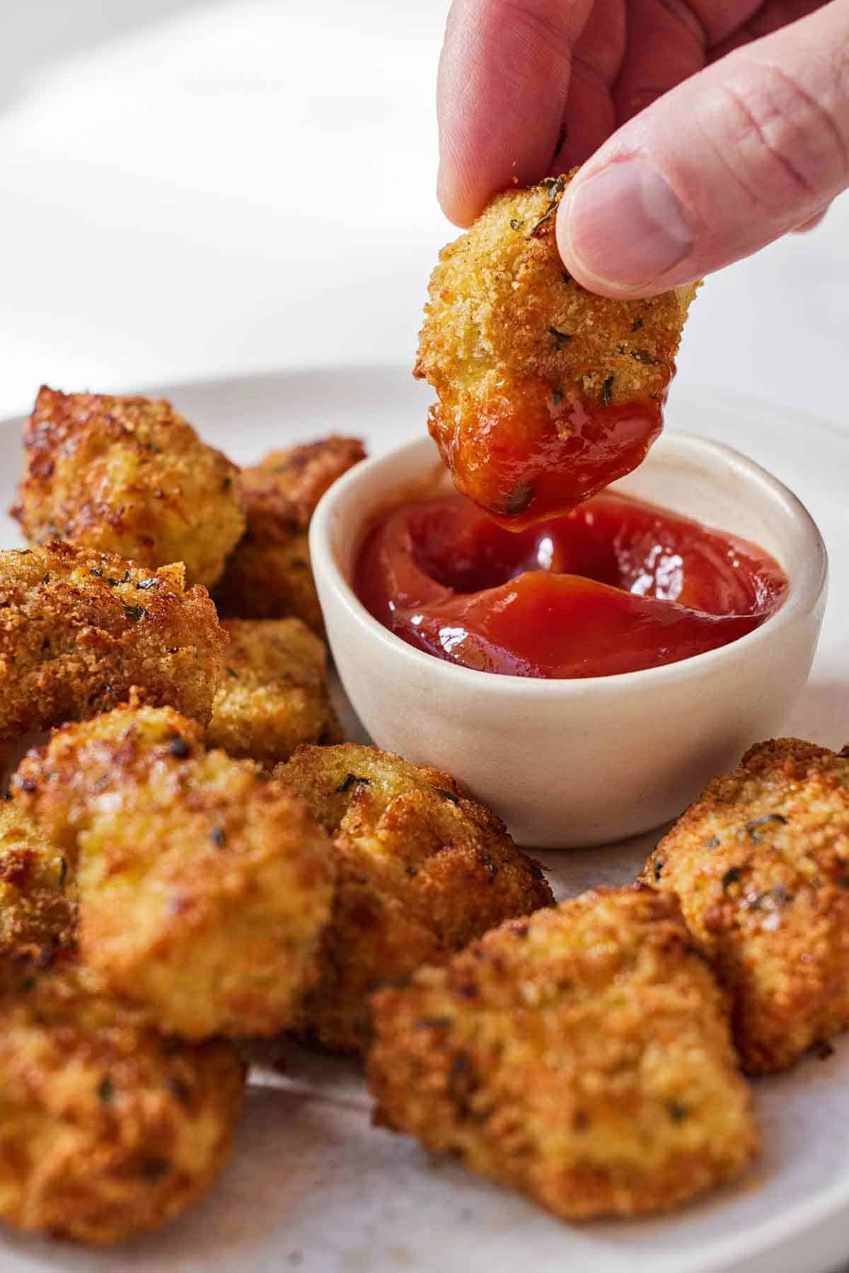 A plate of air fryer chicken nuggets with one being dipped into ketchup.