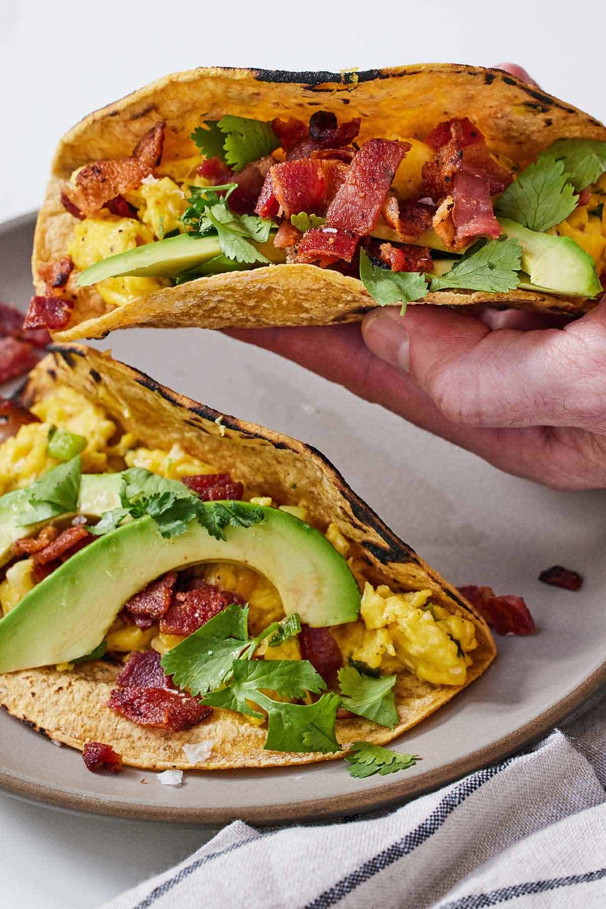 A hand lifting a breakfast taco off a plate.