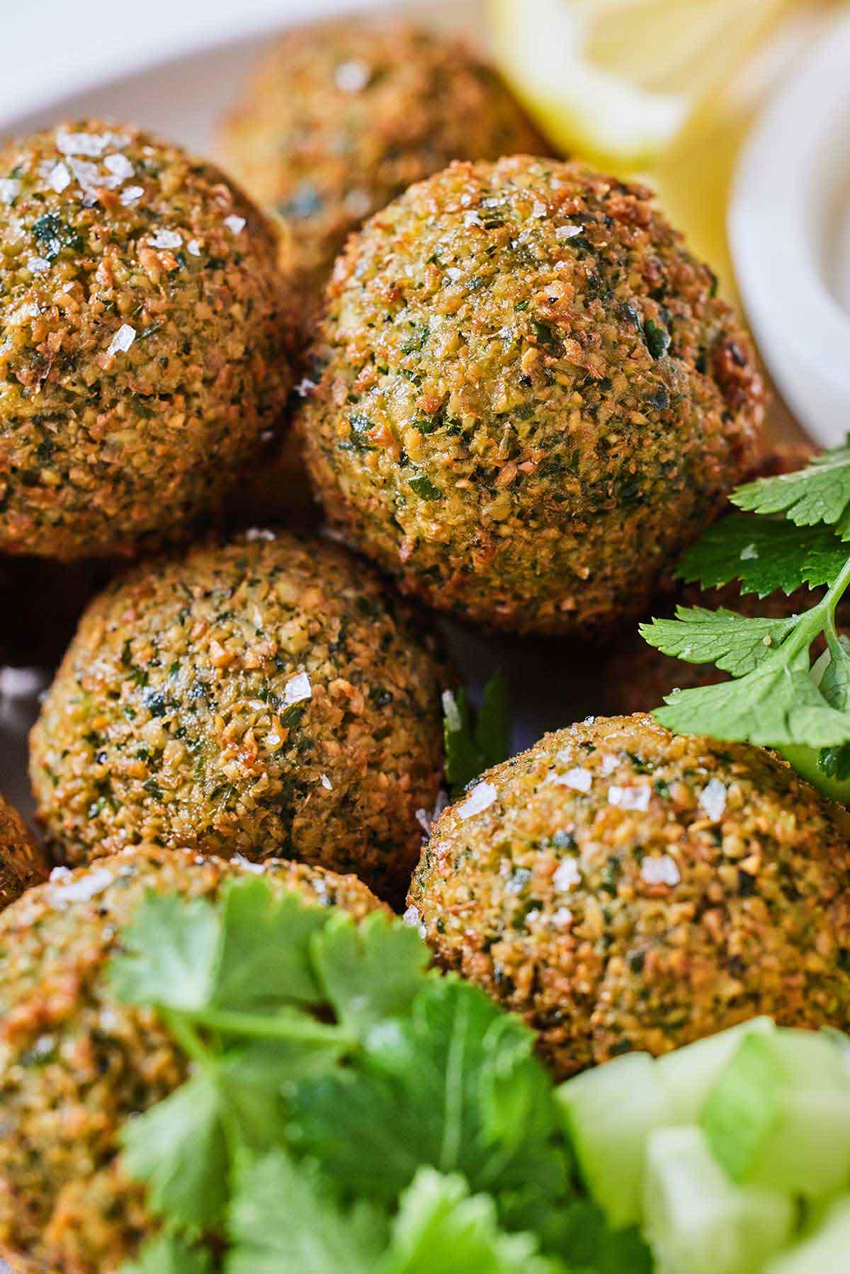Close up of multiple falafels with flaky salt and fresh herbs as garnish.