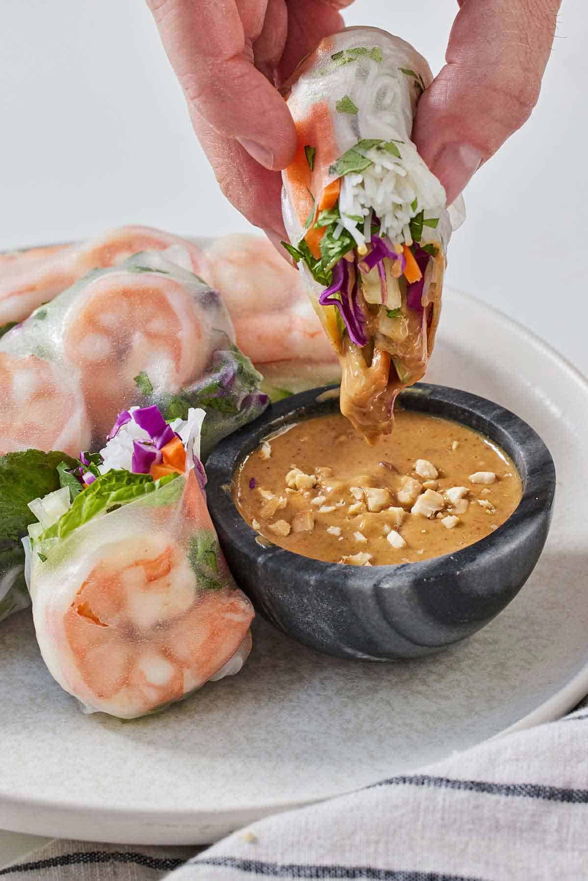 Half of a salad roll dipped into a peanut sauce.
