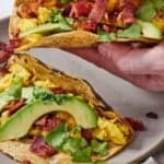 Pinterest graphic of a hand lifting up a breakfast taco from a plate.