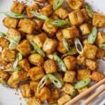 Pinterest graphic of a plate of baked tofu with sesame seeds and green onions.