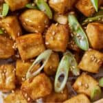 Pinterest graphic of a close view of baked tofu cubes garnished with scallions and sesame seeds.