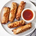 Overhead view of air fryer egg rolls on a plate with dip on the side.