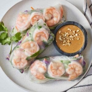 Overhead view of a plate with three salad rolls, cilantro, and peanut sauce.