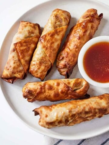 Overhead view of a plate of air fryer egg rolls with a bowl of dipping sauce.