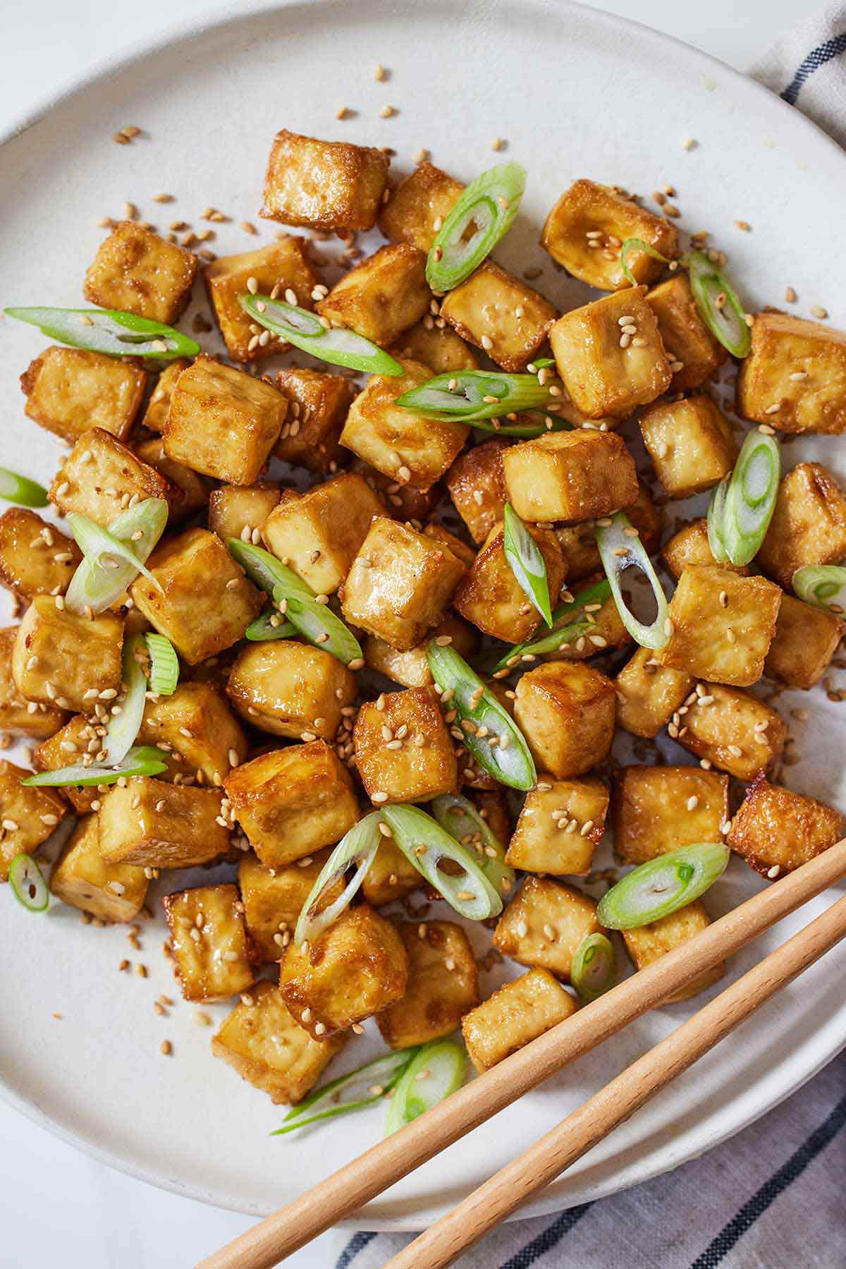 A plate of baked tofu with sesame seeds and scallions on top.