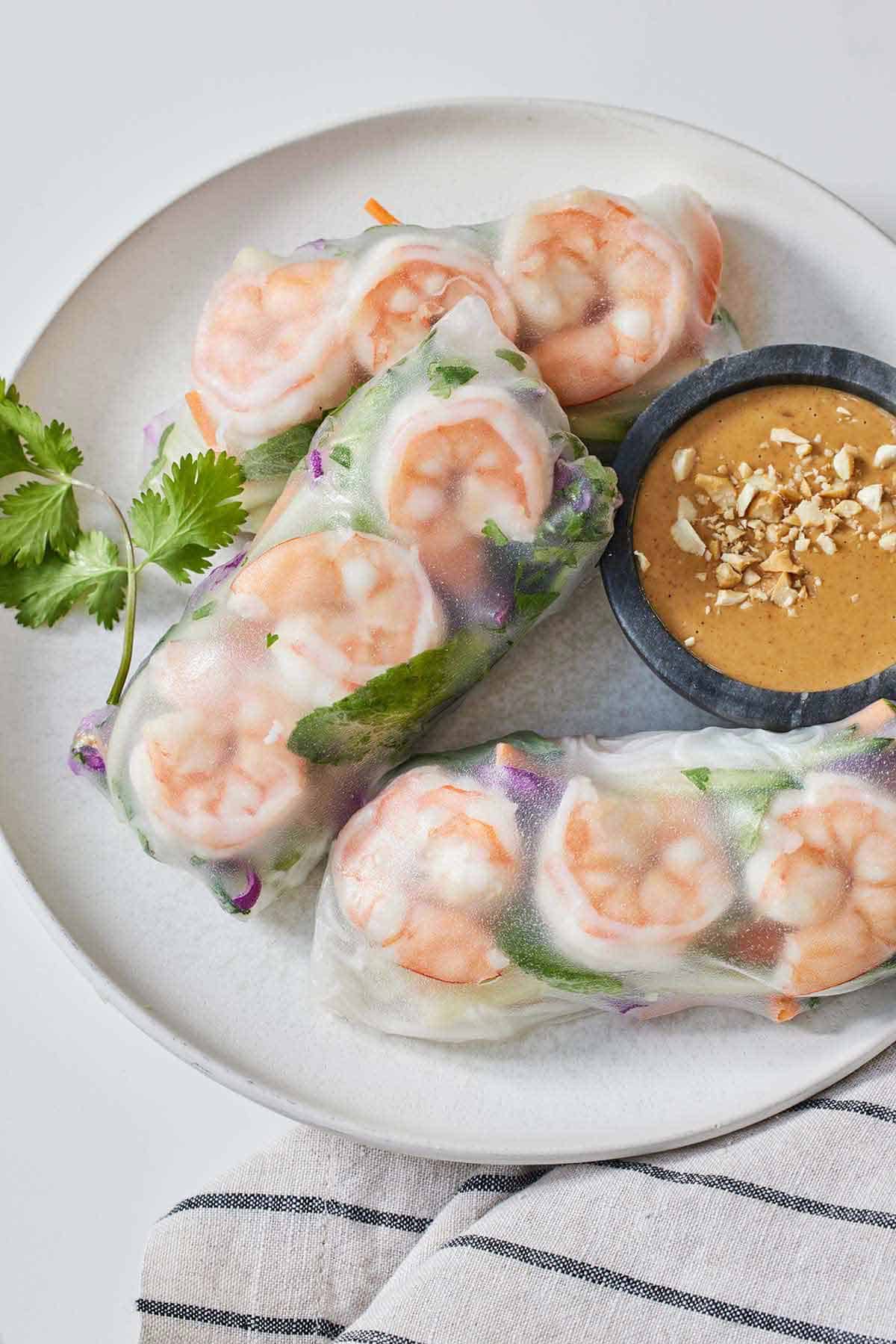 A plate with three salad rolls with a peanut dip on the side.