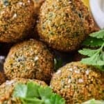 Pinterest graphic of a close view of a pile of falafels with fresh herbs around.
