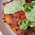 Pinterest graphic of a close up view of one crispy Peruvian chicken thigh with cilantro lime crema and cilantro on top.