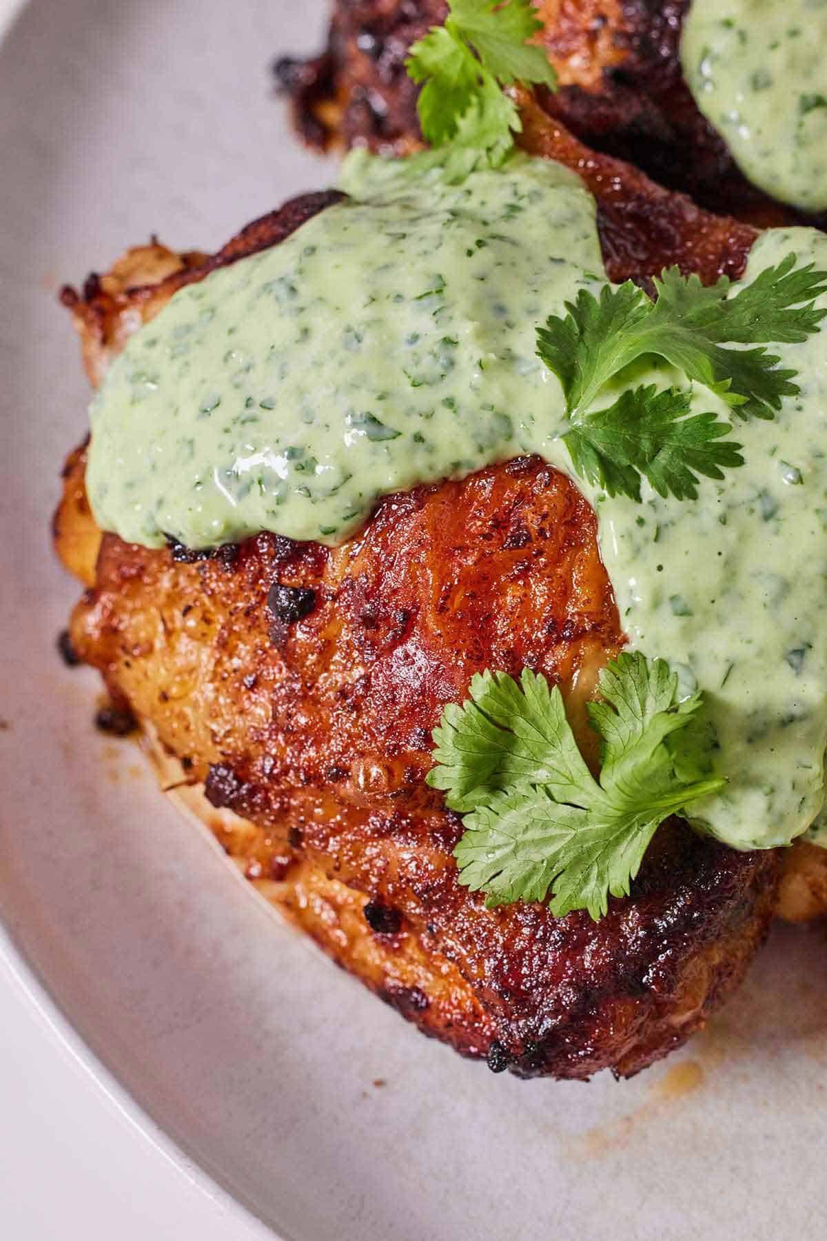 Close up view of a Peruvian chicken thigh with cilantro lime crema sauce on top.