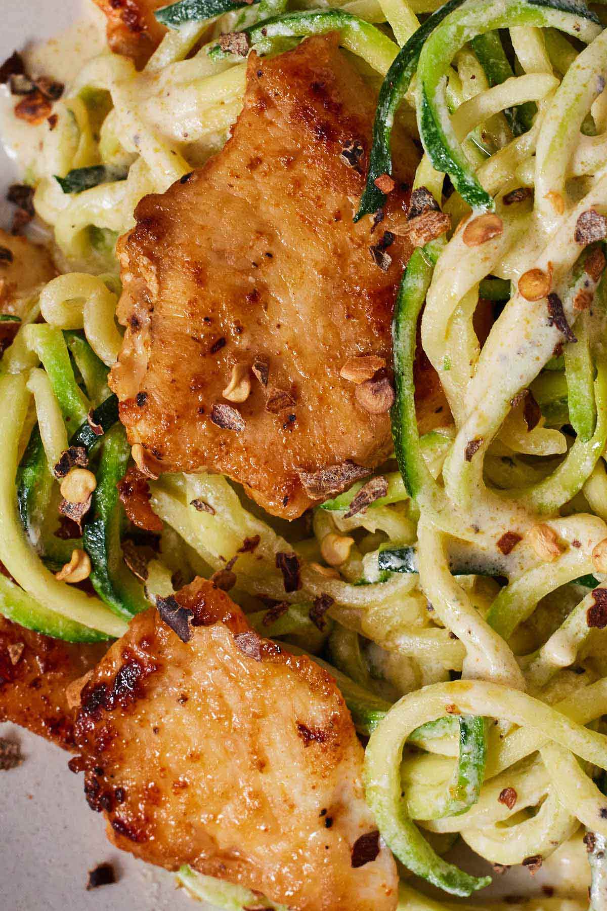 Close up of two pieces of chicken over a bed of zucchini noodles.