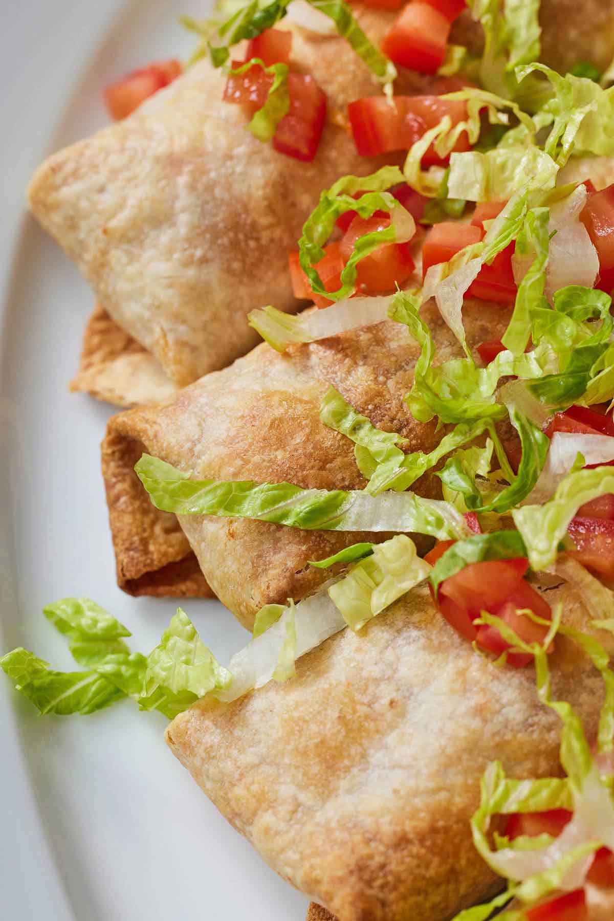 Close up of three chicken chimichangas with shredded lettuce and diced tomatoes on top.