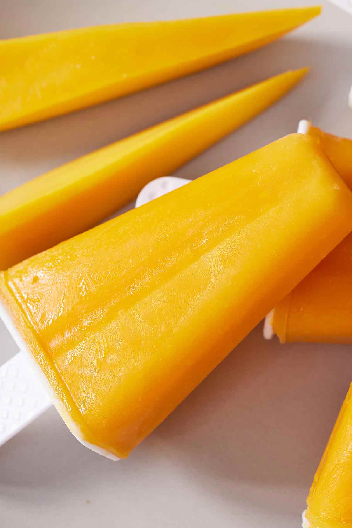 Close up of a mango popsicle beside sliced mangos pieces.
