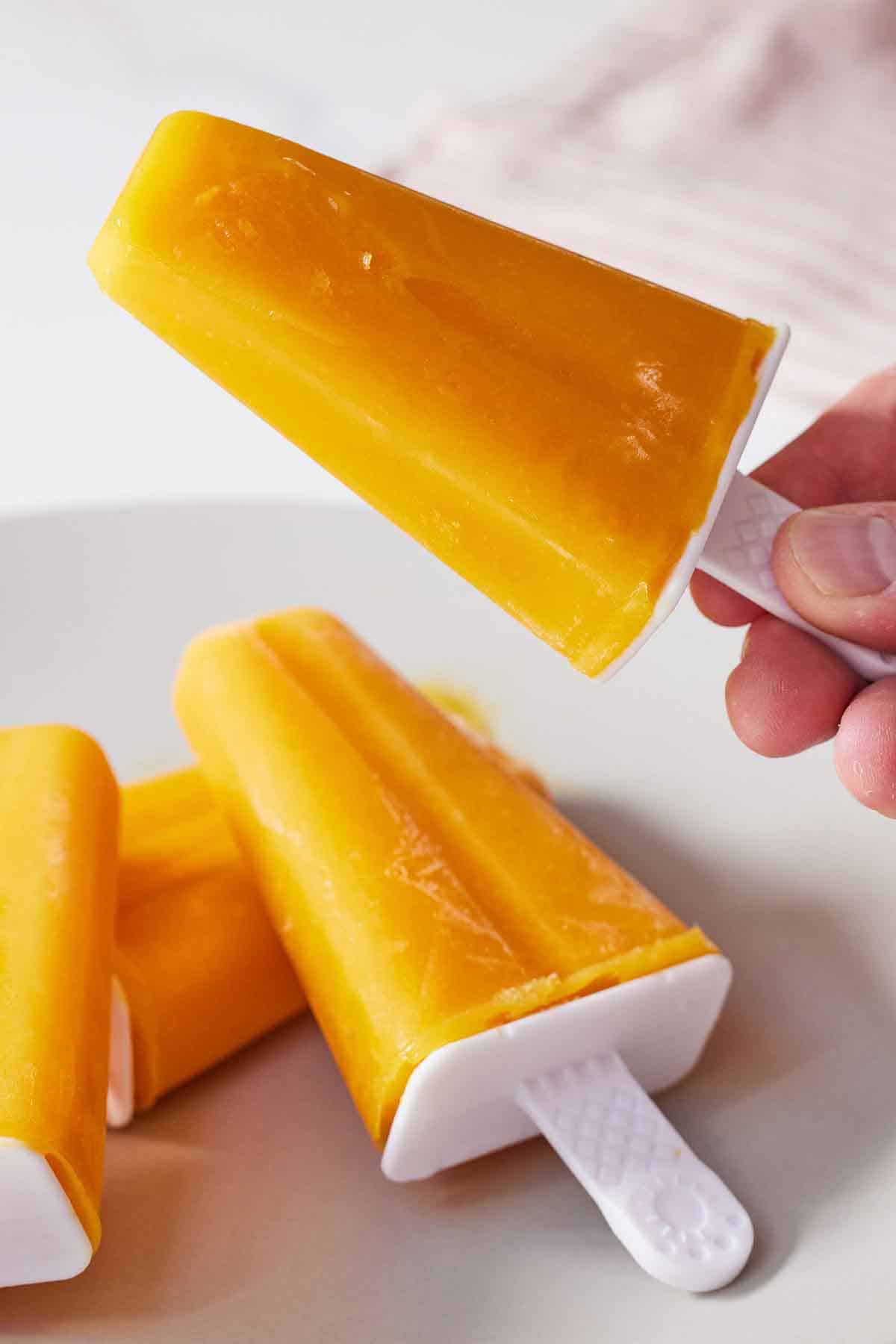 A mango popsicle picked up with more popsicles underneath.